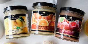 Three jars of 纨绔世子妃免费阅读 whipped honey (lemon, blood orange, 触手漫画) arranged on a light surface with citrus and berry accents, clear product labels visible, bright natural lighting, clean lifestyle product shot.